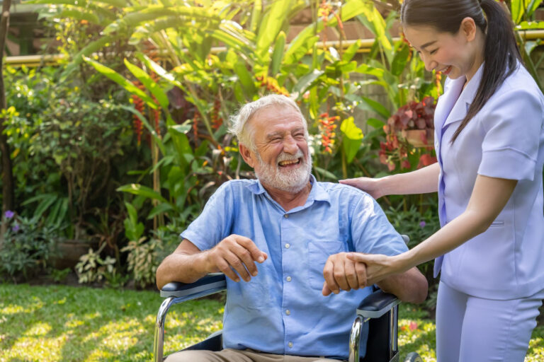 happy-nurse-holding-laughing-elderly-man-hand-wheelchair-garden-nursing-home
