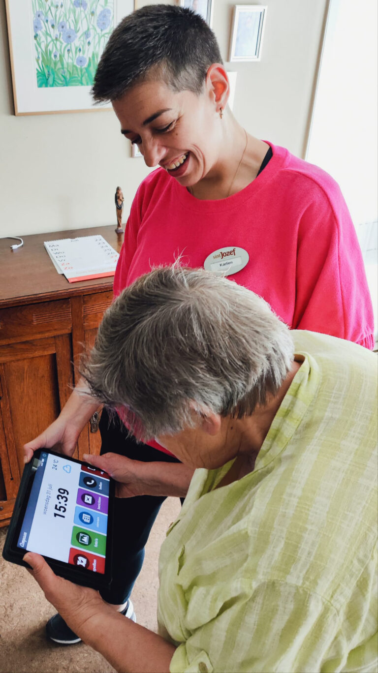 Foto met een zorgmedewerker van Sint Jozef wonen en zorg samen met een bewoner die aan het beeldbellen is middels de Compaan.